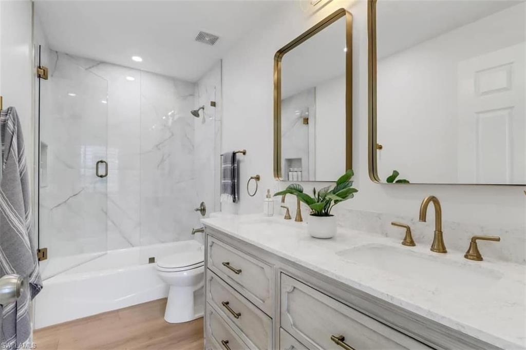 Full bathroom with vanity, toilet, wood-type flooring, and enclosed tub / shower combo