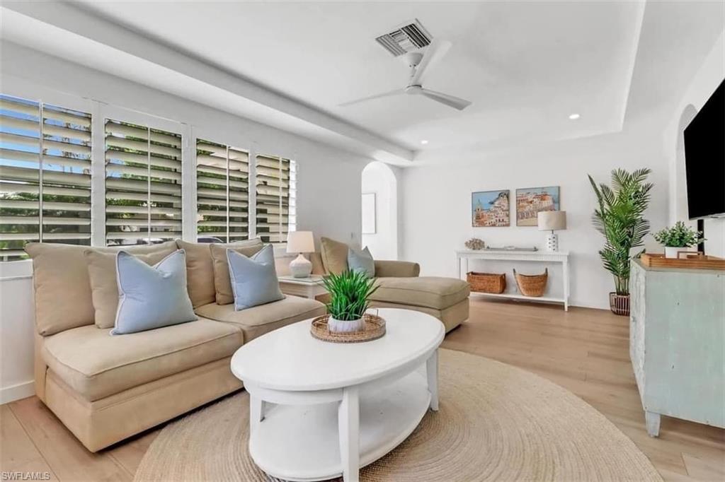 Living room featuring light hardwood / wood-style floors, ceiling fan, and a tray ceiling