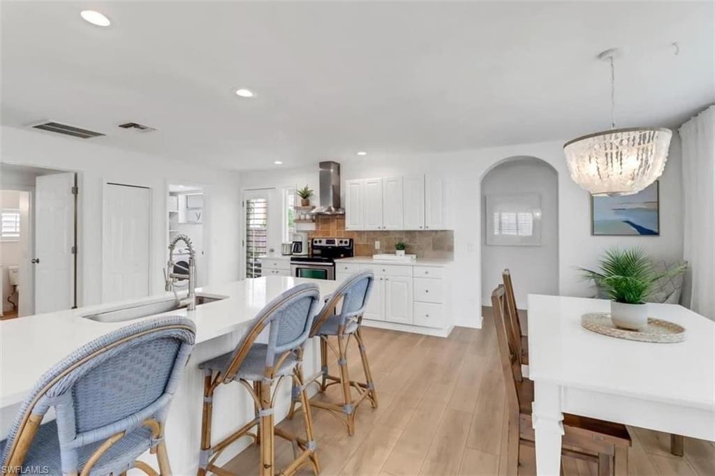 Kitchen featuring stainless steel range with electric cooktop, white cabinets, wall chimney range hood, hanging light fixtures, and a chandelier