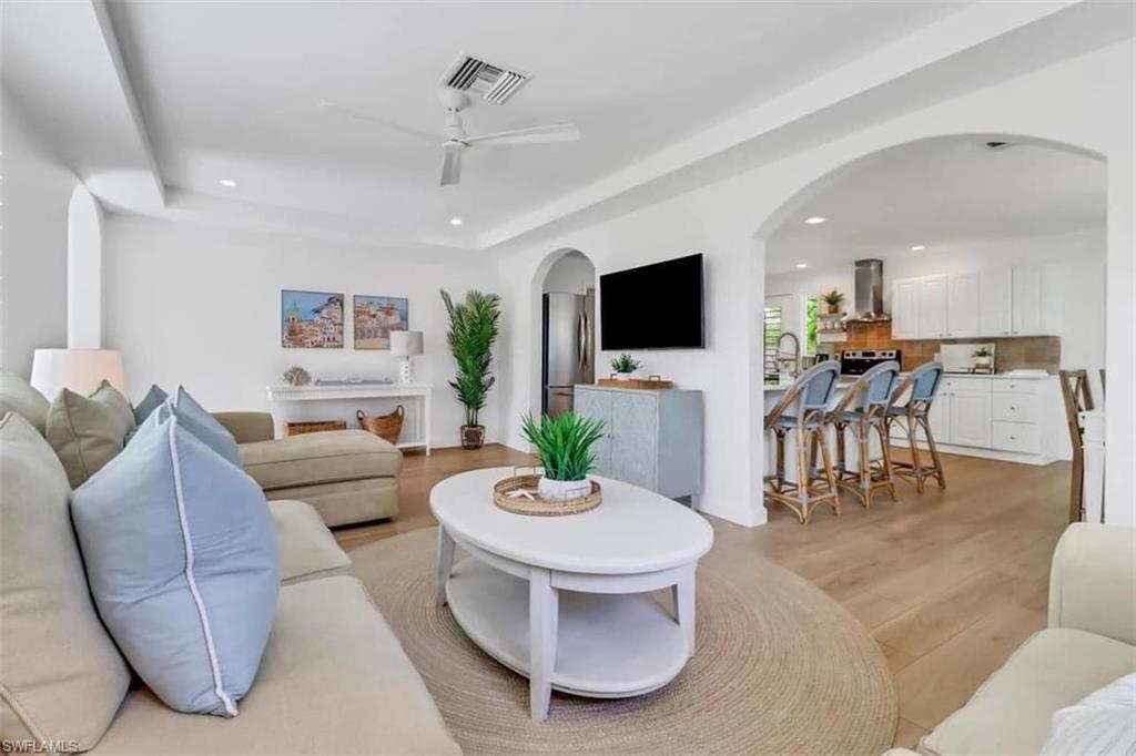 Living room with a tray ceiling, ceiling fan, sink, and light hardwood / wood-style floors