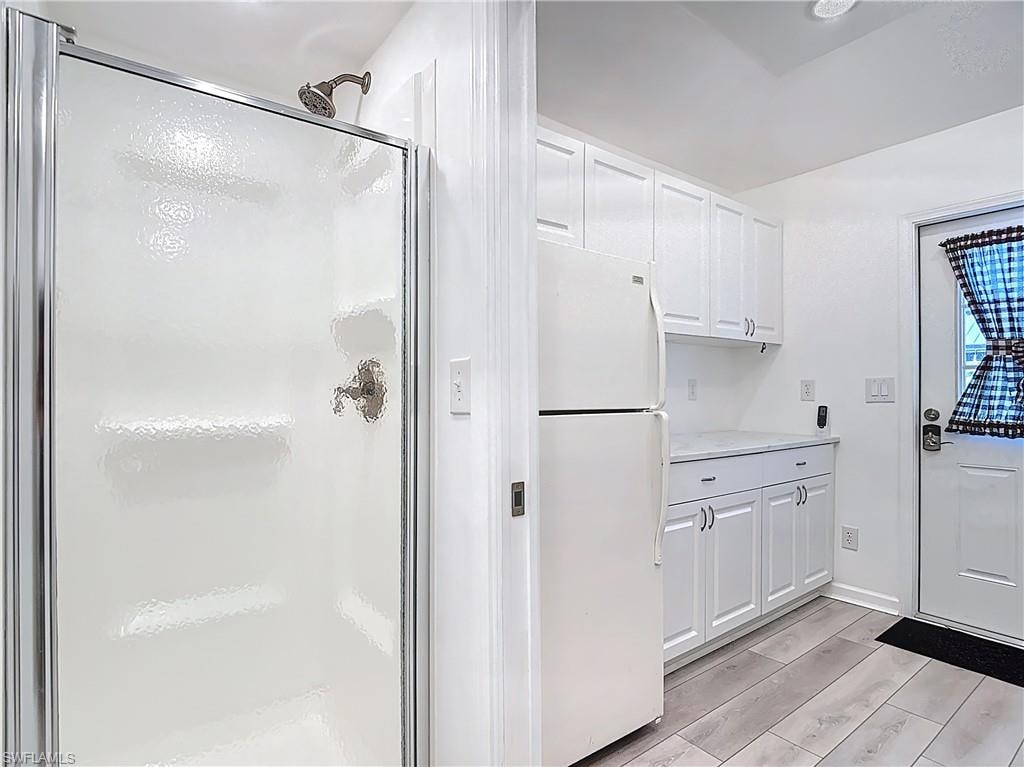 Kitchen featuring white cabinetry, freestanding refrigerator, light countertops, and wood tiled floors