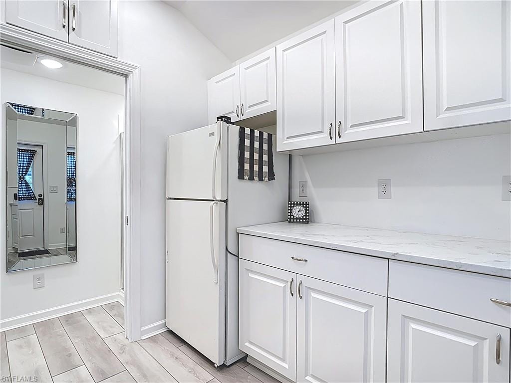Kitchen featuring white cabinetry, light stone countertops, wood finish floors, and freestanding refrigerator