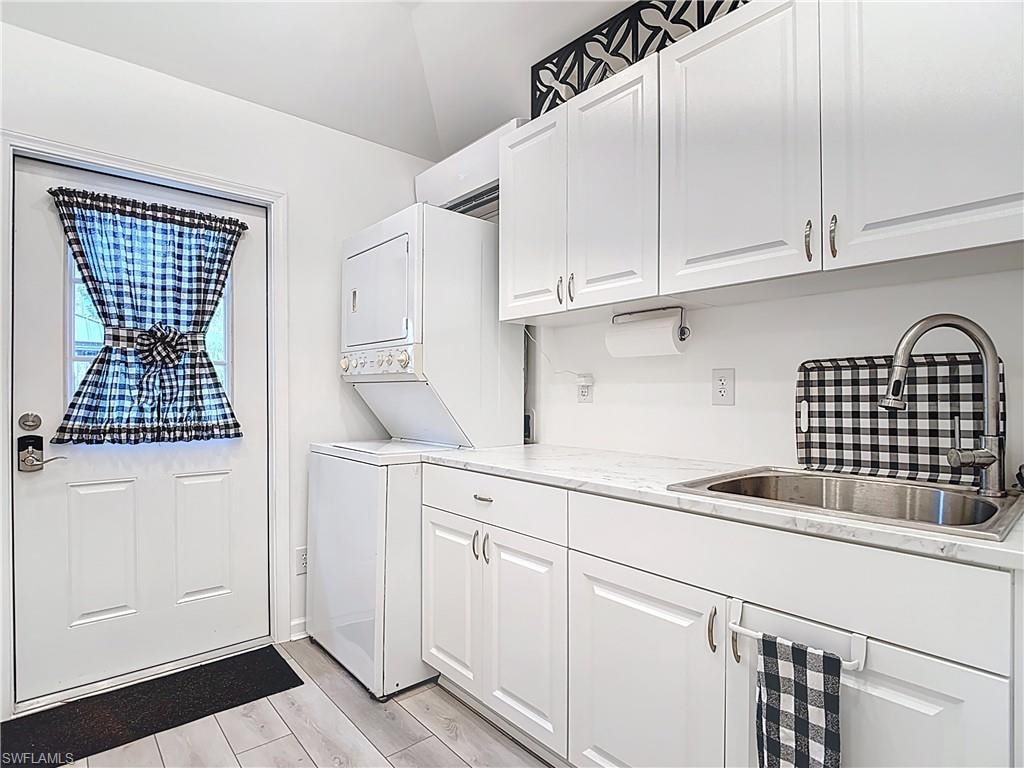 Washroom featuring estacked washer and dryer, light wood-style floors, and cabinet space