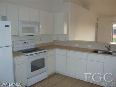 Kitchen featuring white appliances, white cabinets, light countertops, and light tile patterned floors