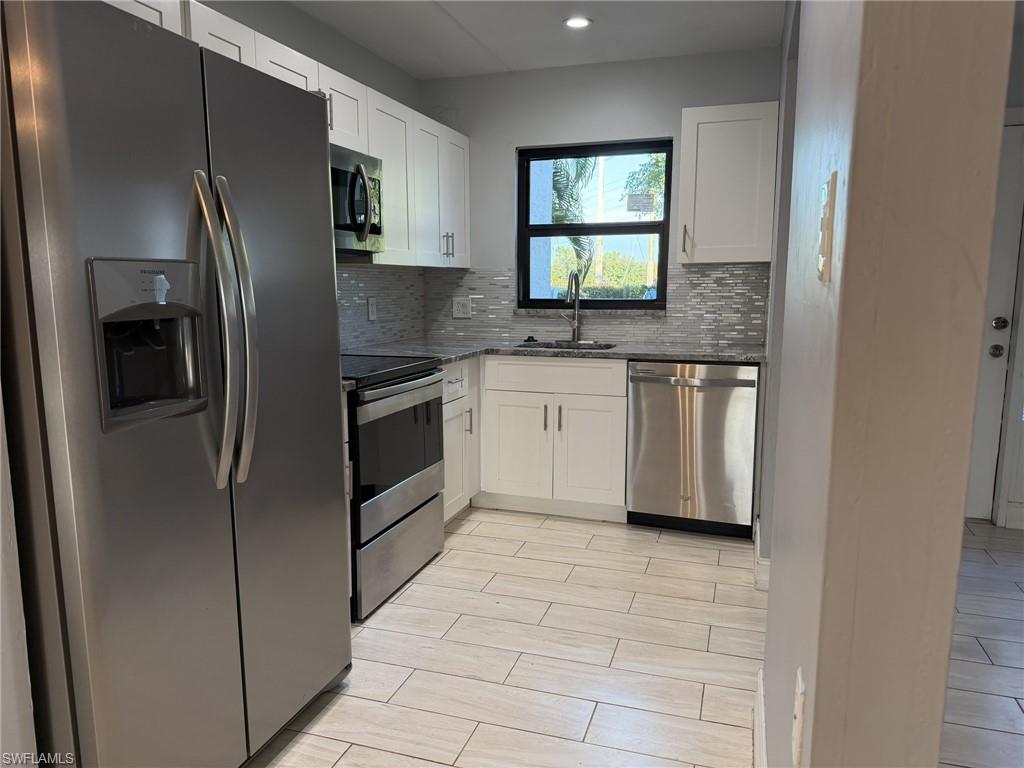 Kitchen with appliances with stainless steel finishes, white cabinetry, dark stone countertops, backsplash, and recessed lighting