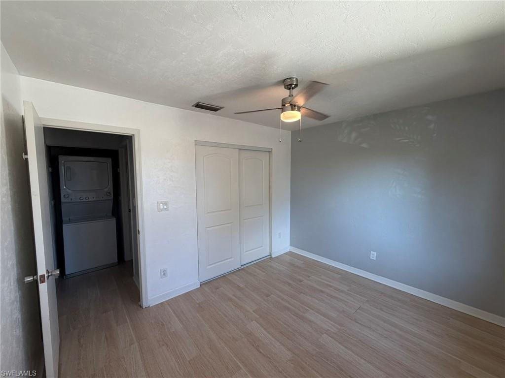 Unfurnished bedroom with stacked washer / drying machine, light wood-type flooring, a closet, ceiling fan, and a textured ceiling