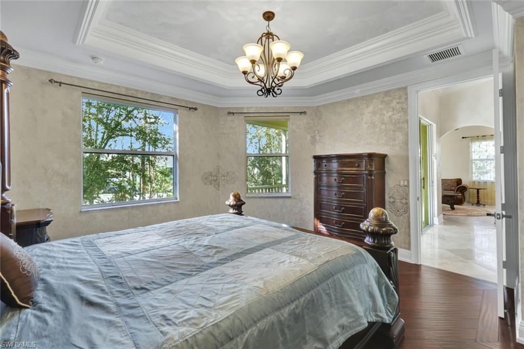 Bedroom featuring dark wood-type flooring, multiple windows, arched walkways, crown molding, and a chandelier