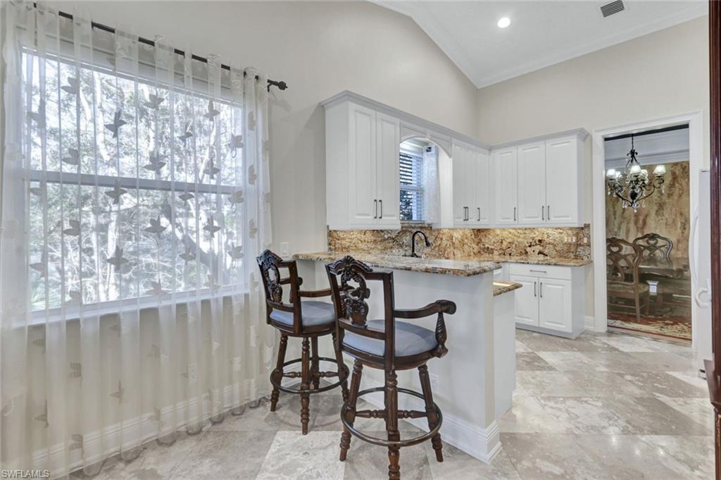 Kitchen featuring vaulted ceiling, white cabinets, light stone counters, a chandelier, and a breakfast bar area