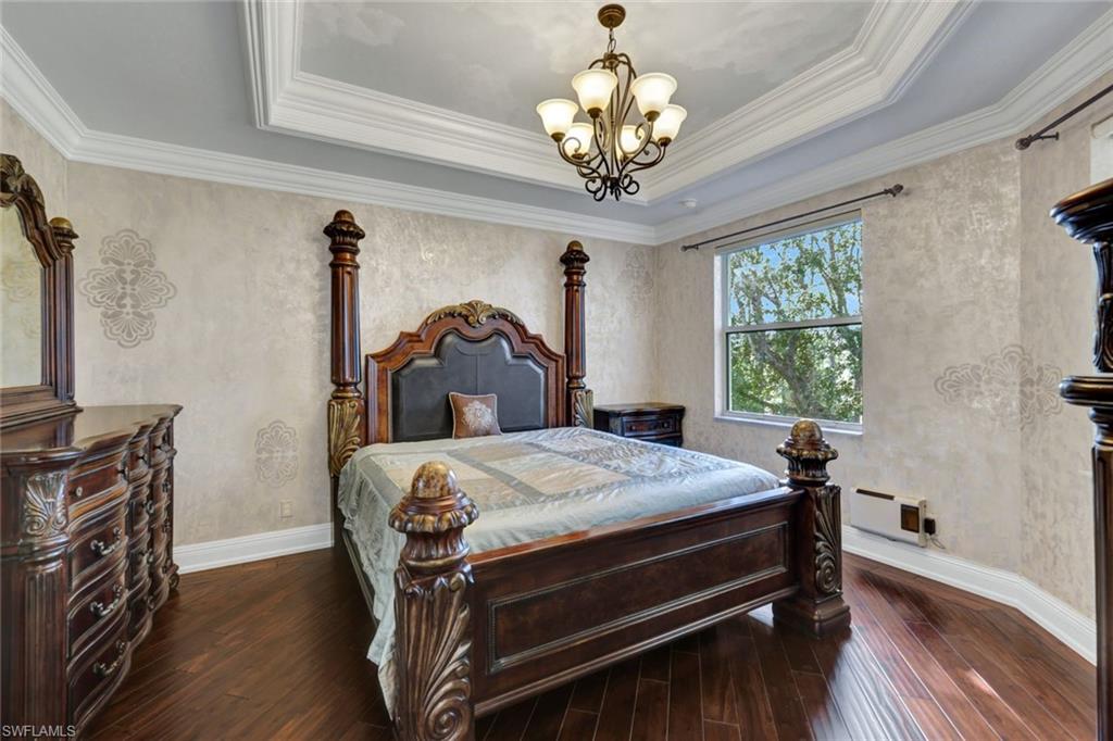 Bedroom with dark wood-style flooring, a chandelier, a raised ceiling, and ornamental molding