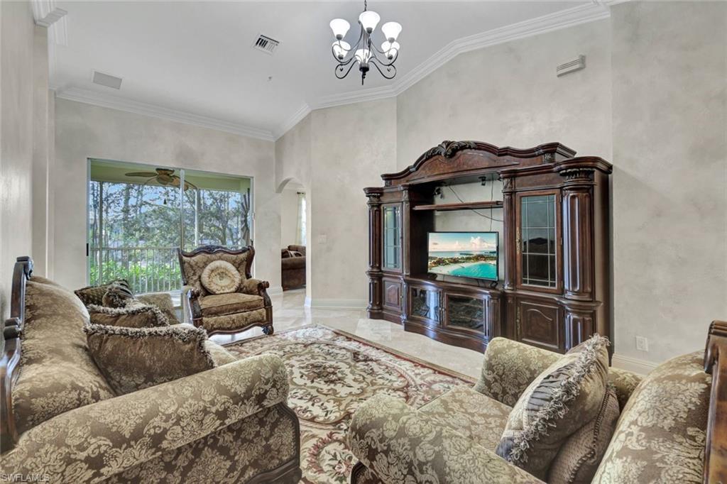 Living area featuring arched walkways, crown molding, marble tiled flooring, a chandelier, and vaulted ceiling