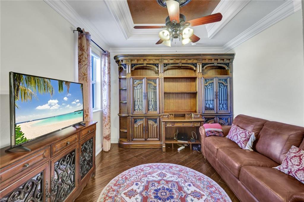 Living area with dark wood-style flooring, ceiling fan, a raised ceiling, and crown molding