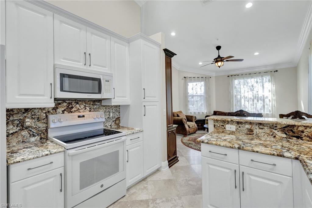 Kitchen featuring white appliances, open floor plan, crown molding, white cabinets, and light stone counters