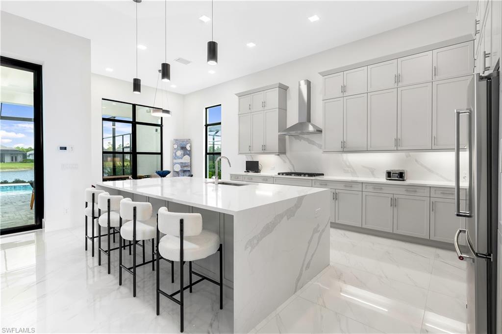 Kitchen with decorative light fixtures, light stone countertops, an island with sink, light marble finish flooring, and a breakfast bar
