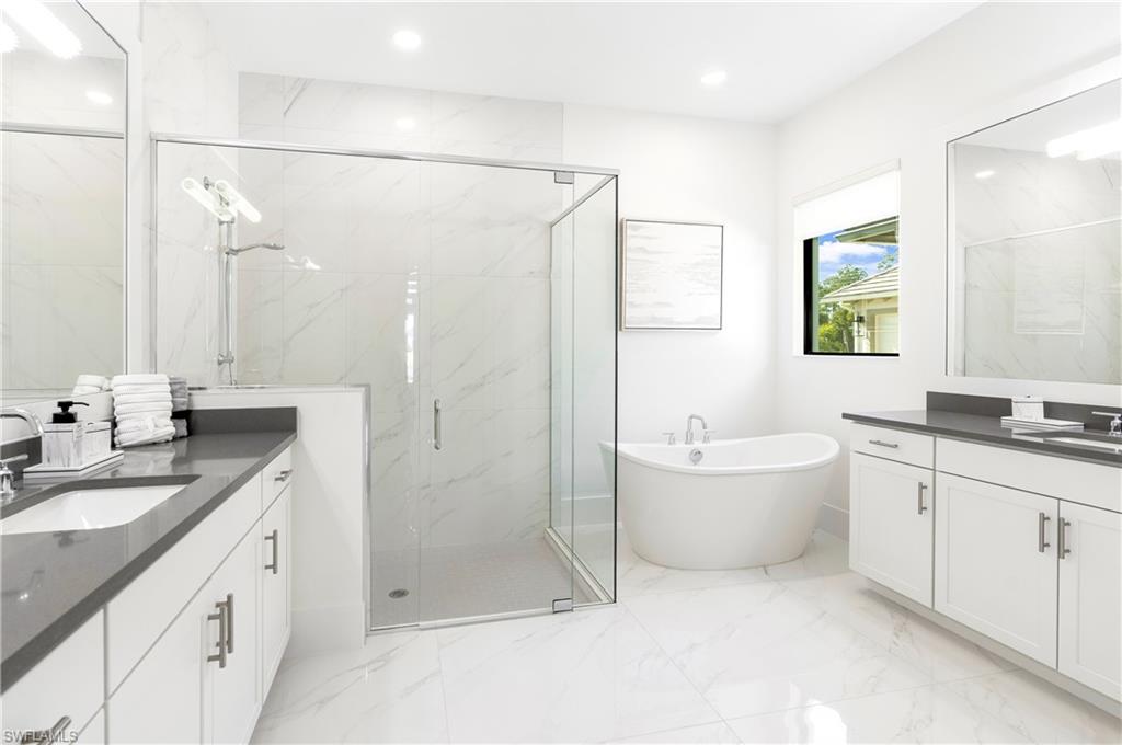 Full bath featuring two vanities, a marble finish shower, a freestanding tub, light marble finish flooring, and recessed lighting