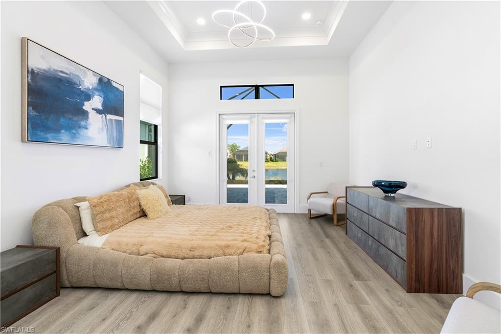 Bedroom with access to exterior, light wood finished floors, french doors, a high ceiling, and a chandelier