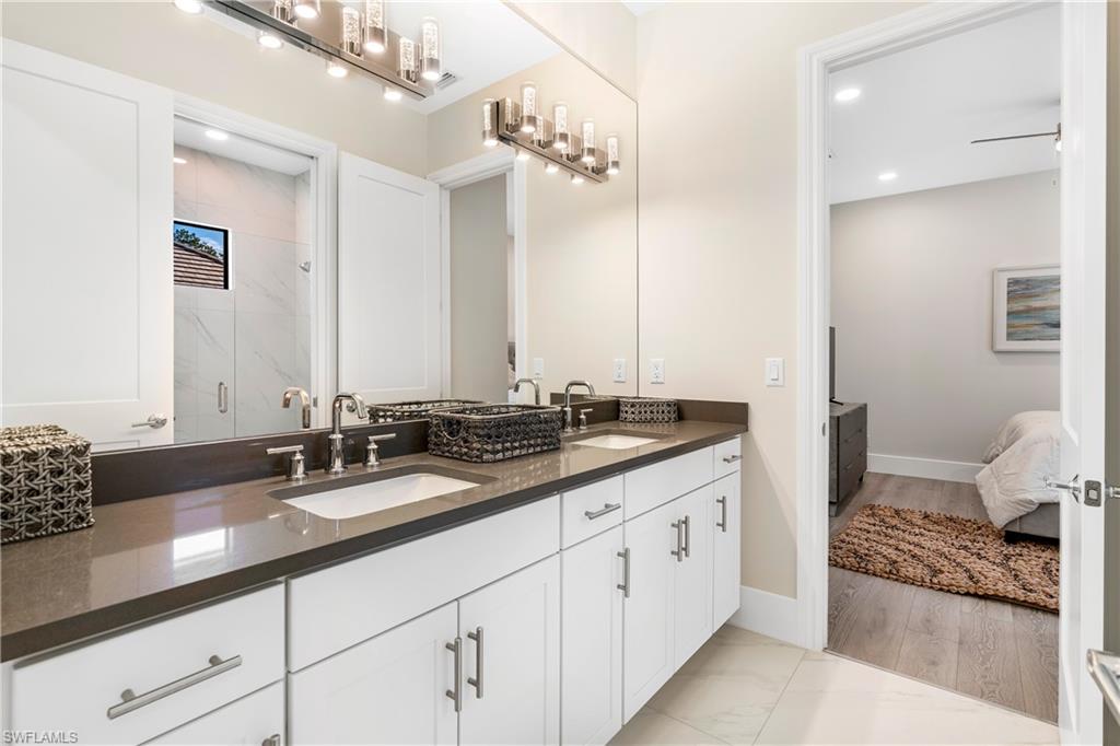 Ensuite bathroom with double vanity, a marble finish shower, light marble finish flooring, and recessed lighting