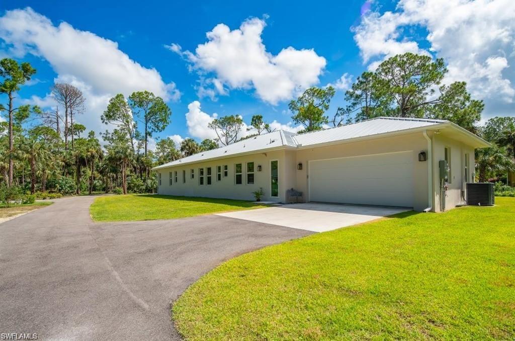 Ranch-style home with driveway, a front lawn, stucco siding, an attached garage, and a metal roof