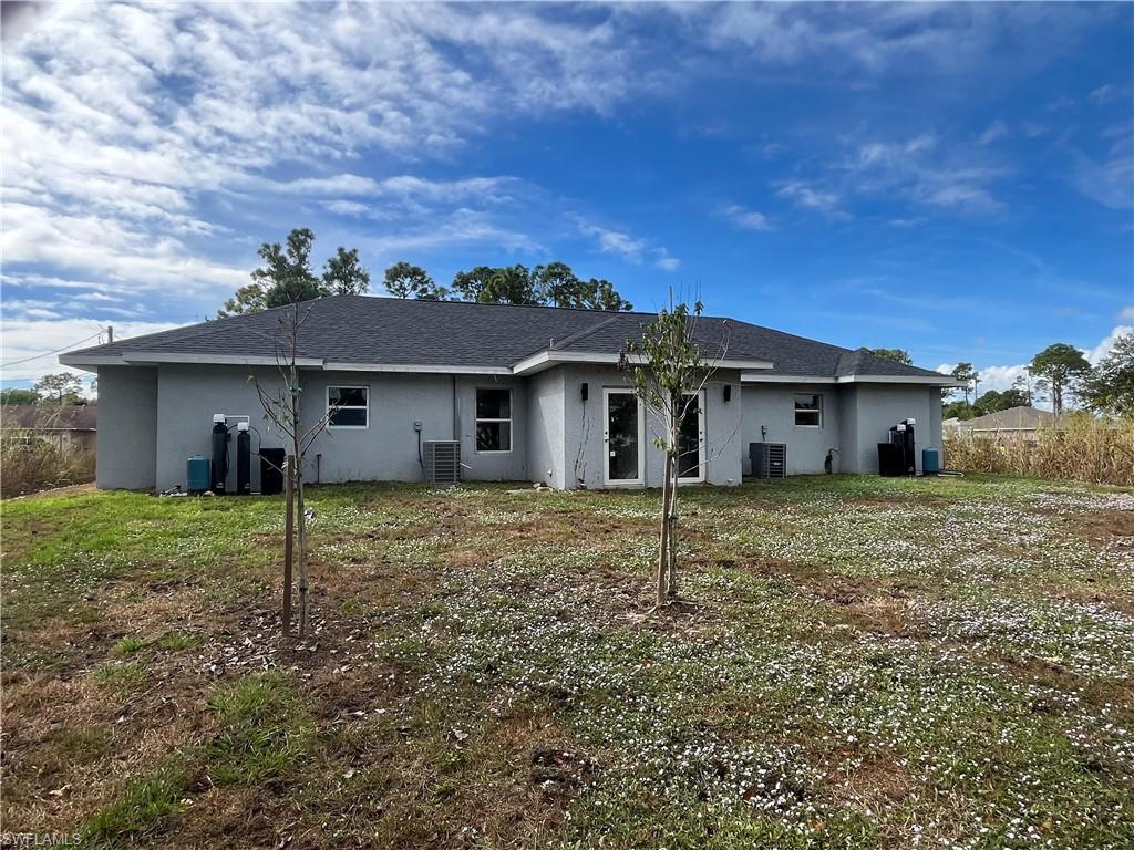 Back of property with stucco siding, a lawn, and a shingled roof