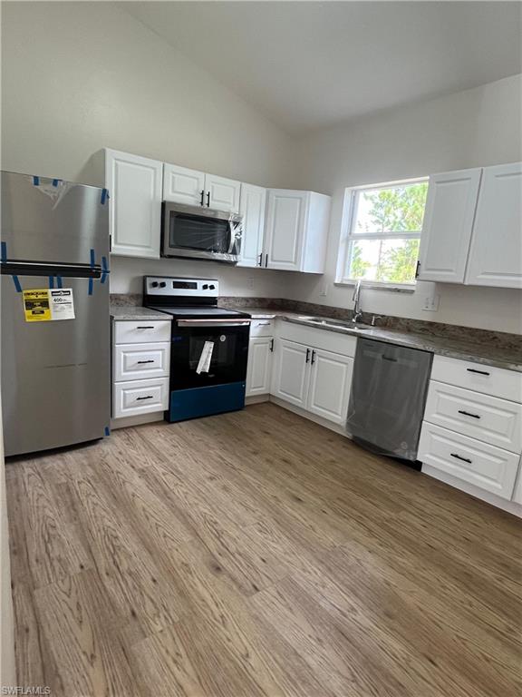 Kitchen featuring appliances with stainless steel finishes, white cabinets, vaulted ceiling, and light wood finished floors