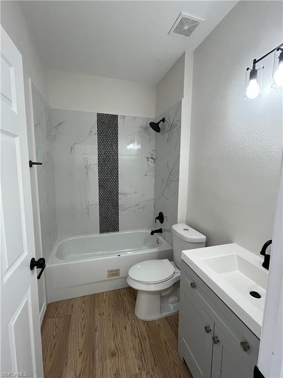 Full bath with bathing tub / shower combination, vanity, light wood-style floors, and a textured wall