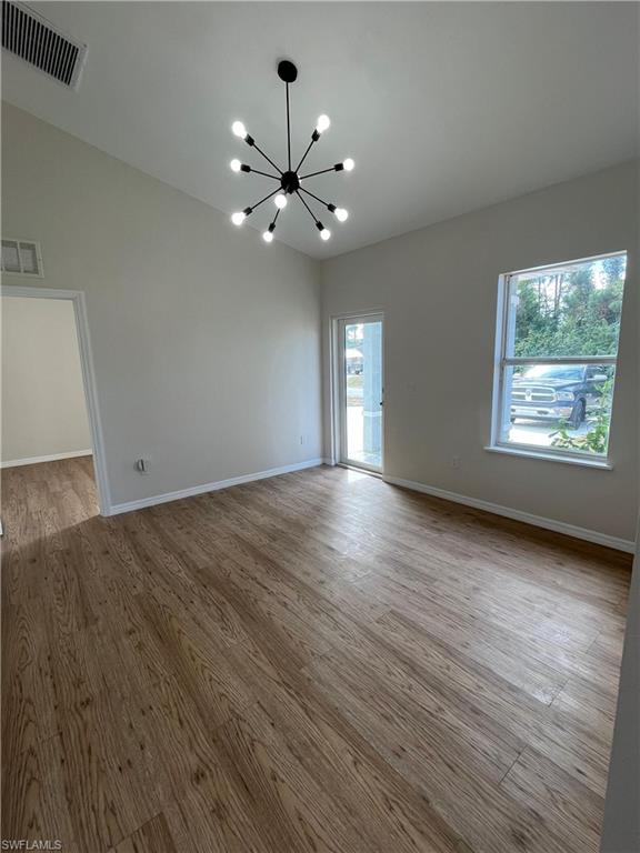 Spare room with a chandelier, light wood-type flooring, and vaulted ceiling