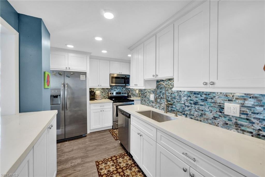 Kitchen featuring white cabinetry, stainless steel appliances, backsplash, recessed lighting, and light wood-type flooring