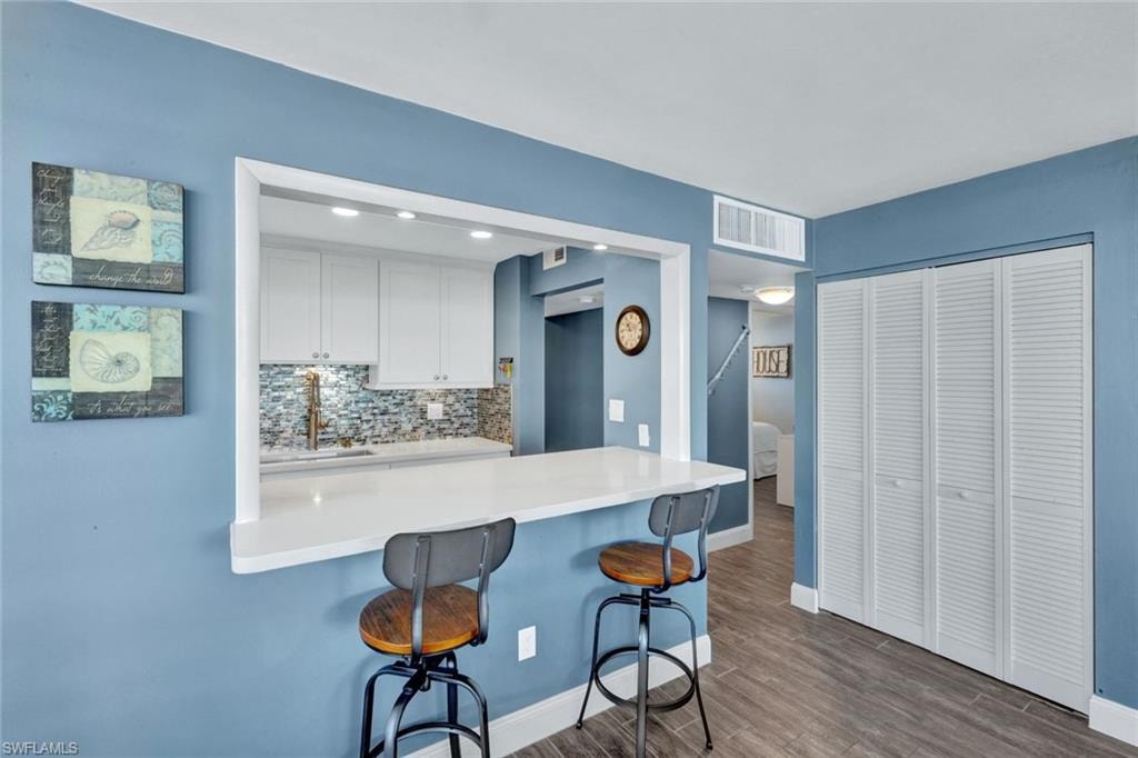 Kitchen featuring white cabinetry, tasteful backsplash, a kitchen breakfast bar, a peninsula, and dark wood finished floors