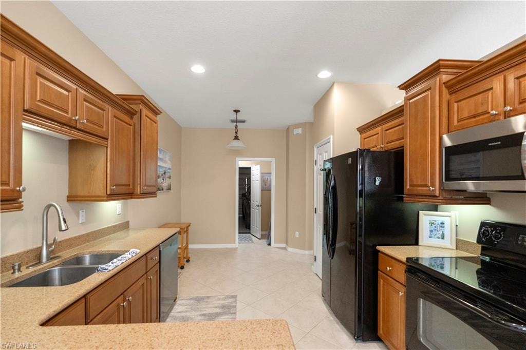 Kitchen featuring appliances with stainless steel finishes, brown cabinetry, decorative light fixtures, light stone counters, and recessed lighting