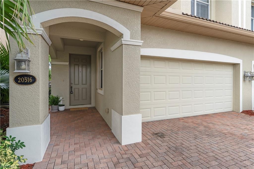 Doorway to property with a garage, stucco siding, and decorative driveway