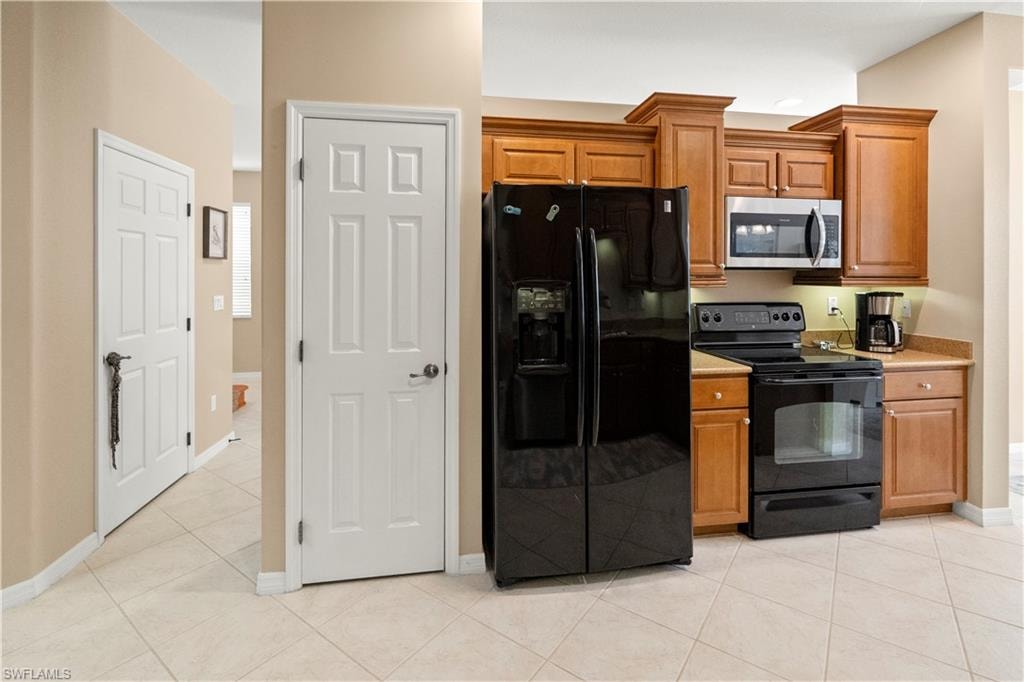 Kitchen featuring black appliances, light countertops, brown cabinetry, and light tile patterned floors