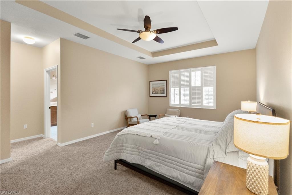 Bedroom featuring a tray ceiling, light carpet, and ceiling fan
