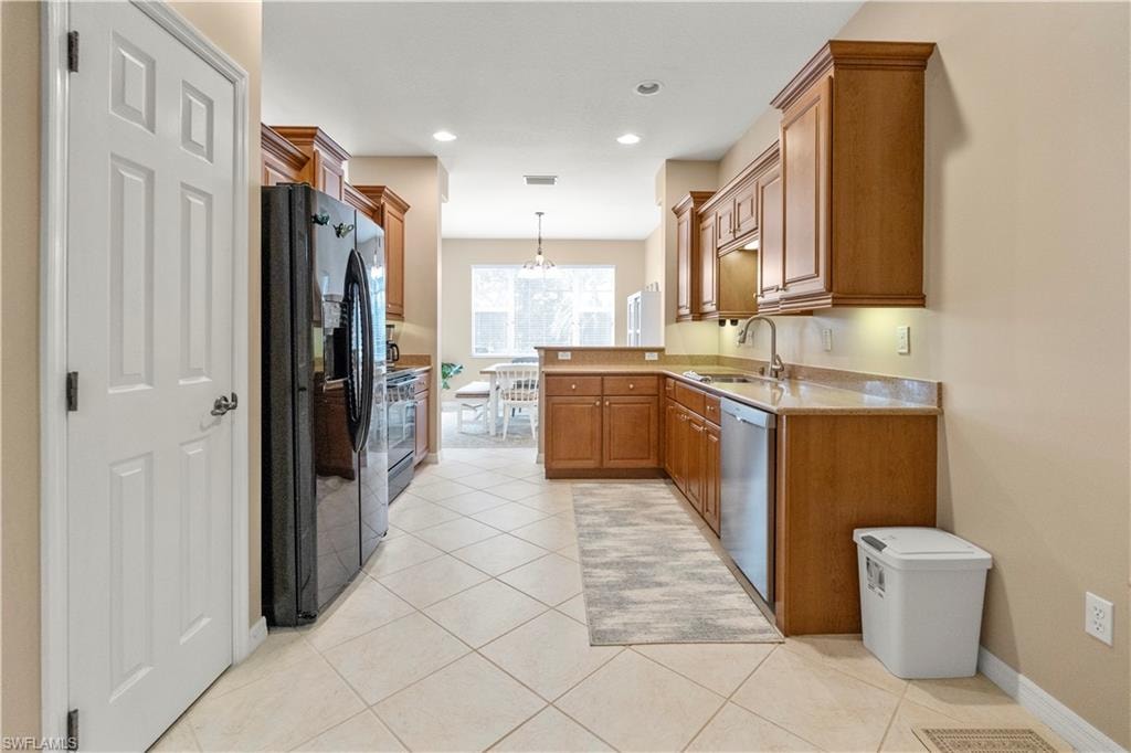 Kitchen with stainless steel appliances, decorative light fixtures, brown cabinets, light tile patterned floors, and a peninsula