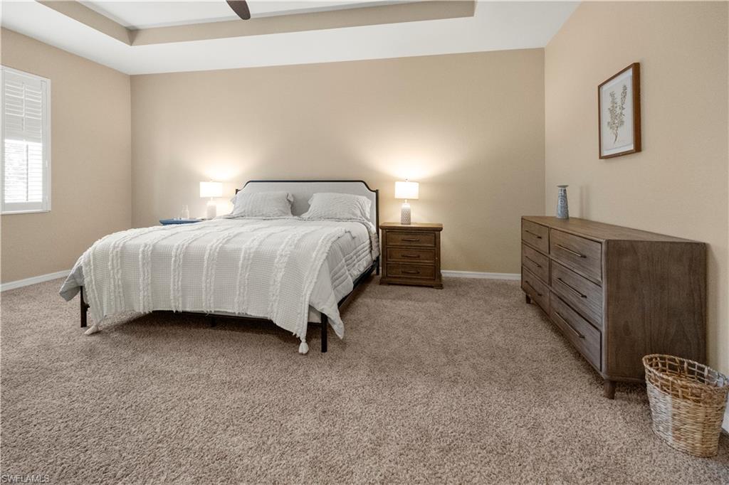 Bedroom with a raised ceiling, light carpet, and ceiling fan
