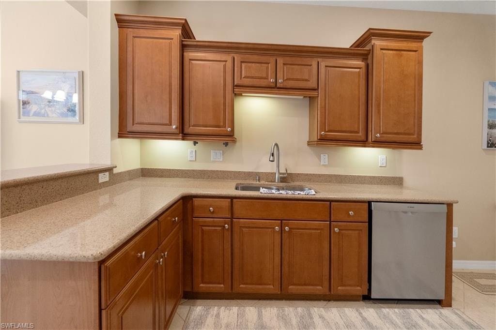 Kitchen featuring brown cabinets, dishwasher, and light stone counters