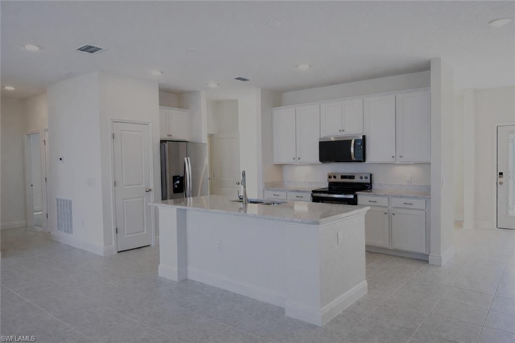 Kitchen featuring stainless steel appliances, white cabinetry, an island with sink, light stone countertops, and recessed lighting