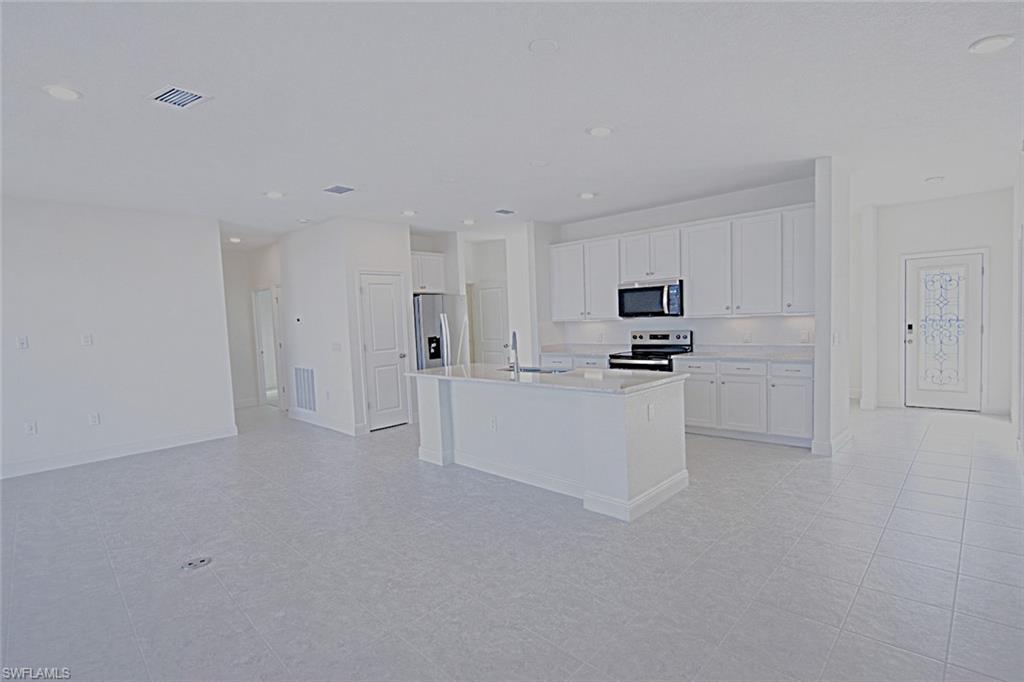 Kitchen featuring white cabinetry, stainless steel appliances, a kitchen island with sink, recessed lighting, and light stone countertops