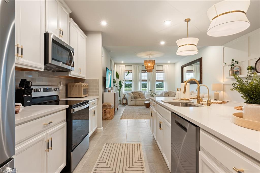 Kitchen featuring stainless steel appliances, white cabinets, tasteful backsplash, decorative light fixtures, and open floor plan