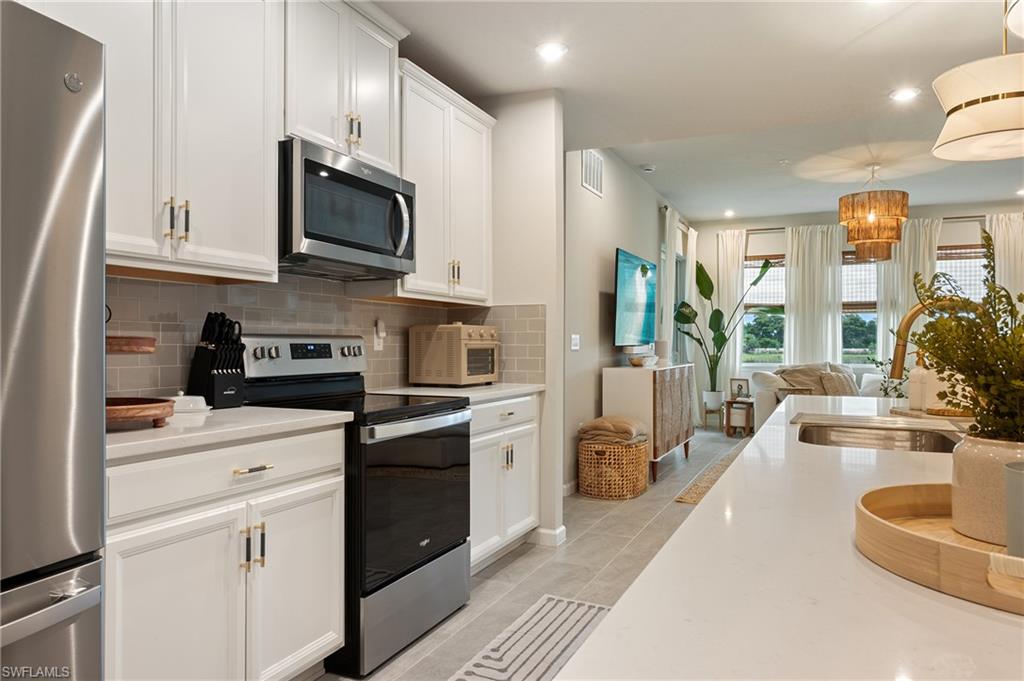 Kitchen featuring appliances with stainless steel finishes, tasteful backsplash, white cabinets, light stone counters, and recessed lighting
