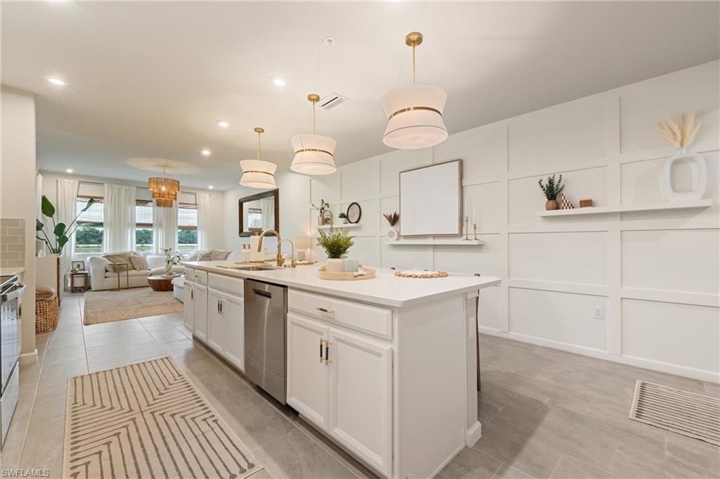 Kitchen with a center island with sink, a decorative wall, open floor plan, pendant lighting, and white cabinetry