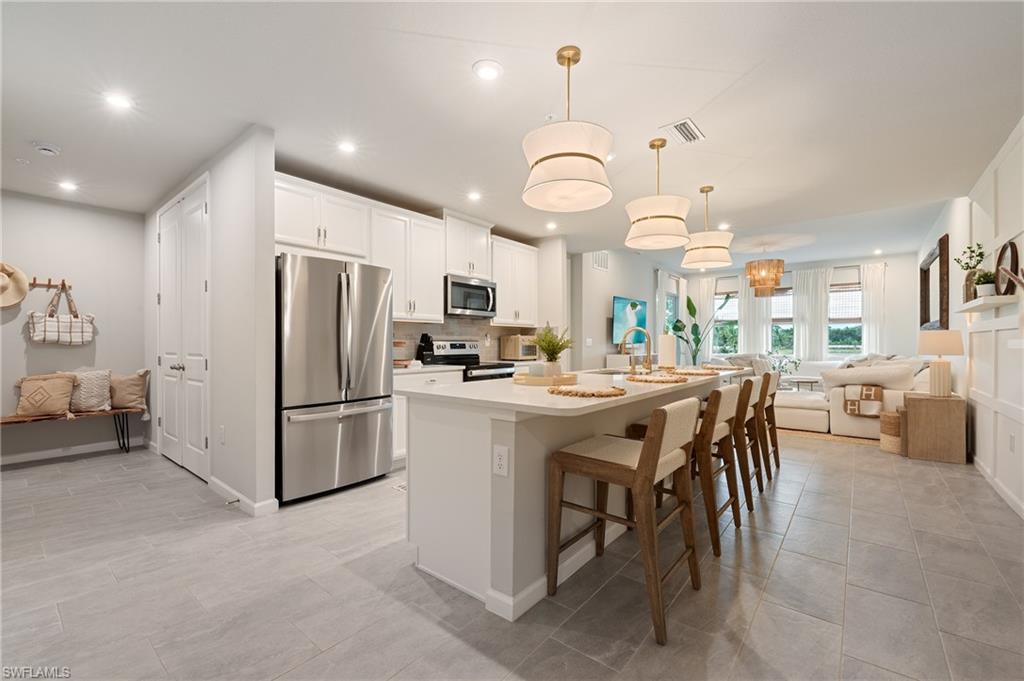 Kitchen featuring open floor plan, appliances with stainless steel finishes, a kitchen island with sink, a kitchen bar, and white cabinets