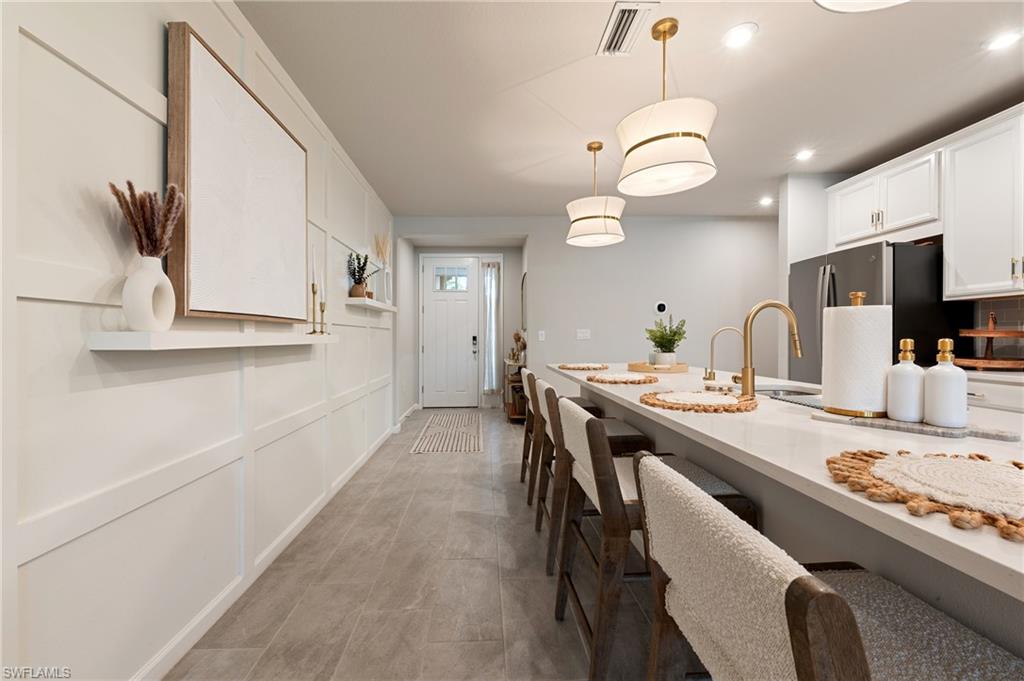 Kitchen with hanging light fixtures, white cabinets, freestanding refrigerator, a decorative wall, and recessed lighting