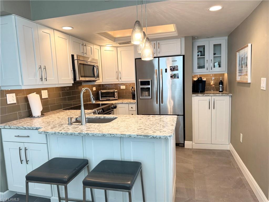 Kitchen with tasteful backsplash, appliances with stainless steel finishes, white cabinets, glass insert cabinets, and an eat in Kitchen