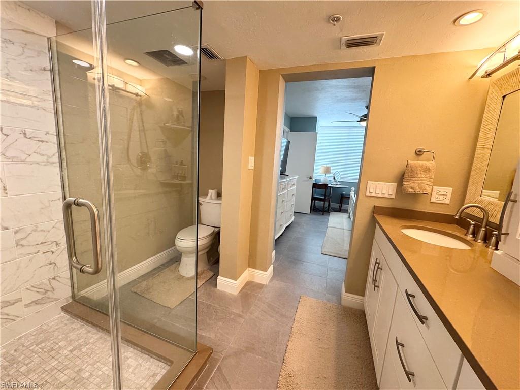 Ensuite bathroom featuring vanity, a stall shower, a textured ceiling, light tile patterned floors, and ceiling fan