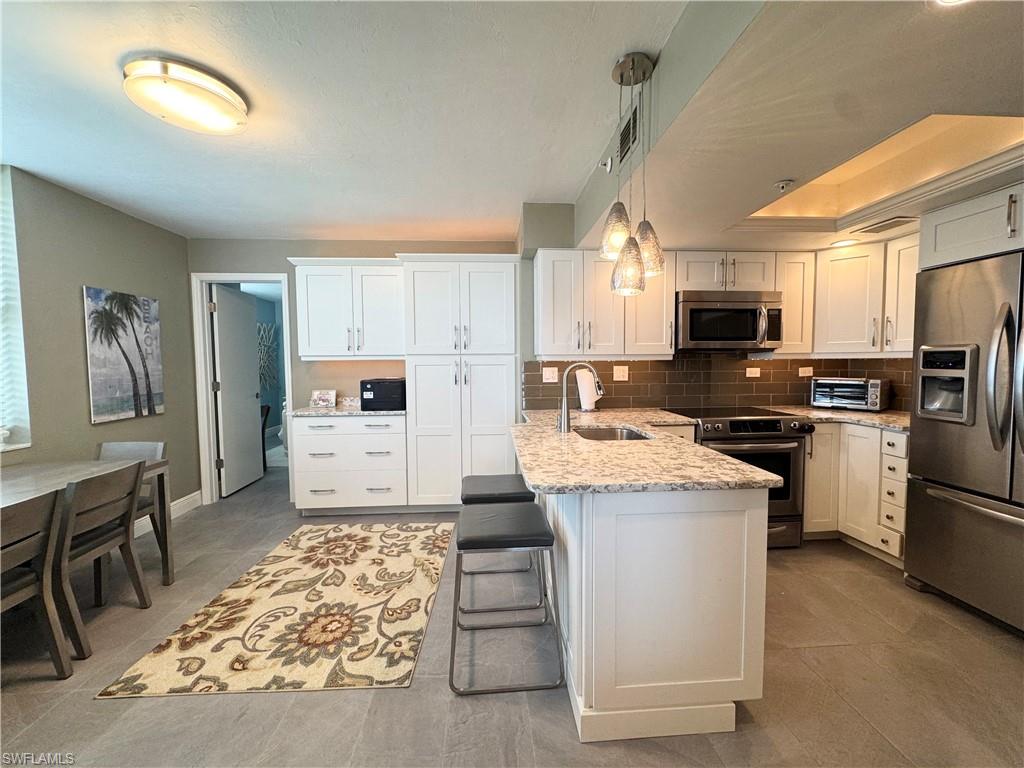 Kitchen featuring appliances with stainless steel finishes, a breakfast bar area, white cabinets, and hanging light fixtures