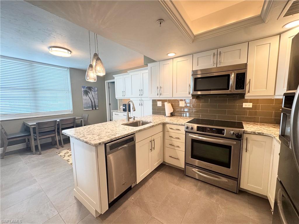 Kitchen featuring appliances with stainless steel finishes, a peninsula, white cabinets, and decorative light fixtures