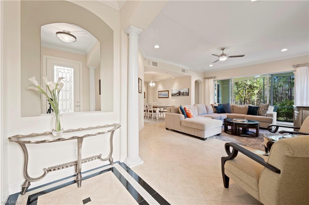 Living area with arched walkways, crown molding, inlaid floor details, light tile patterned flooring, and ornate columns