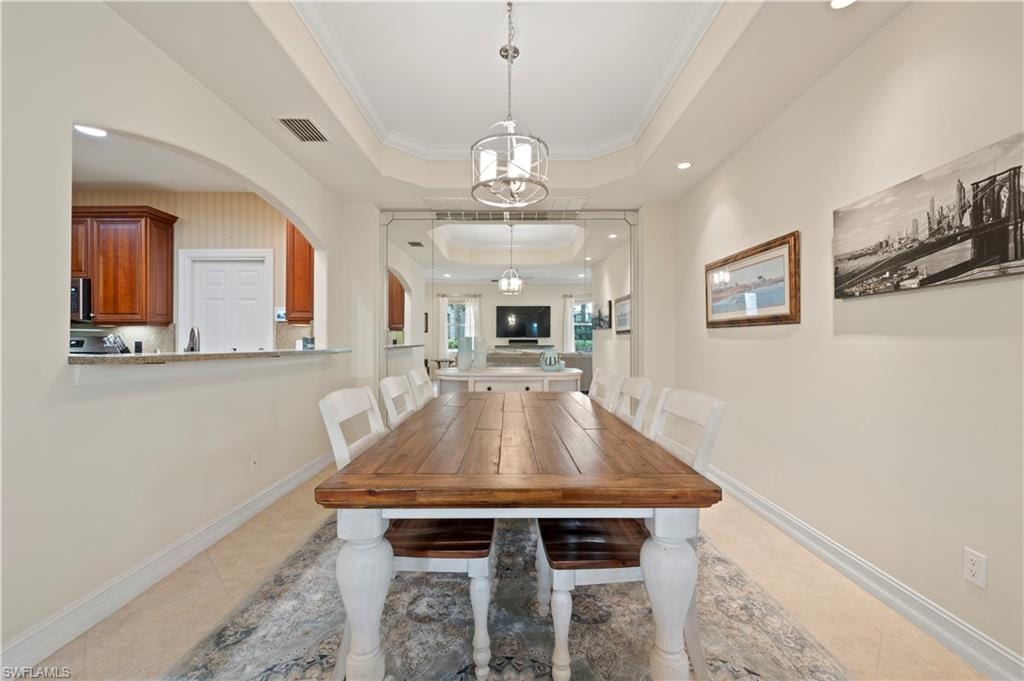 Dining room featuring a raised ceiling, crown molding, light tile patterned flooring, recessed lighting, and arched walkways