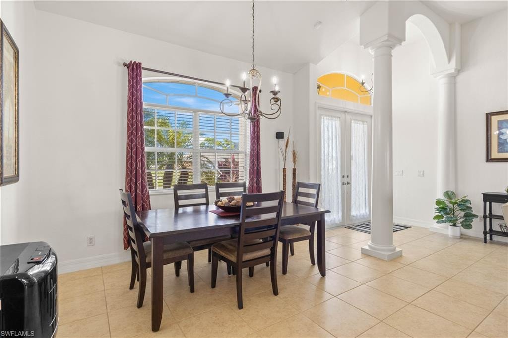 Dining room with decorative columns, french doors, light tile patterned floors, a chandelier, and high vaulted ceiling