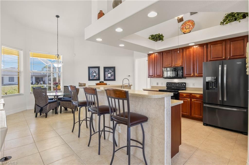 Kitchen featuring black appliances, light countertops, a breakfast bar, hanging light fixtures, and recessed lighting