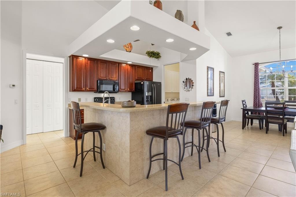 Kitchen featuring a high ceiling, a kitchen bar, black appliances, light tile patterned flooring, and decorative light fixtures